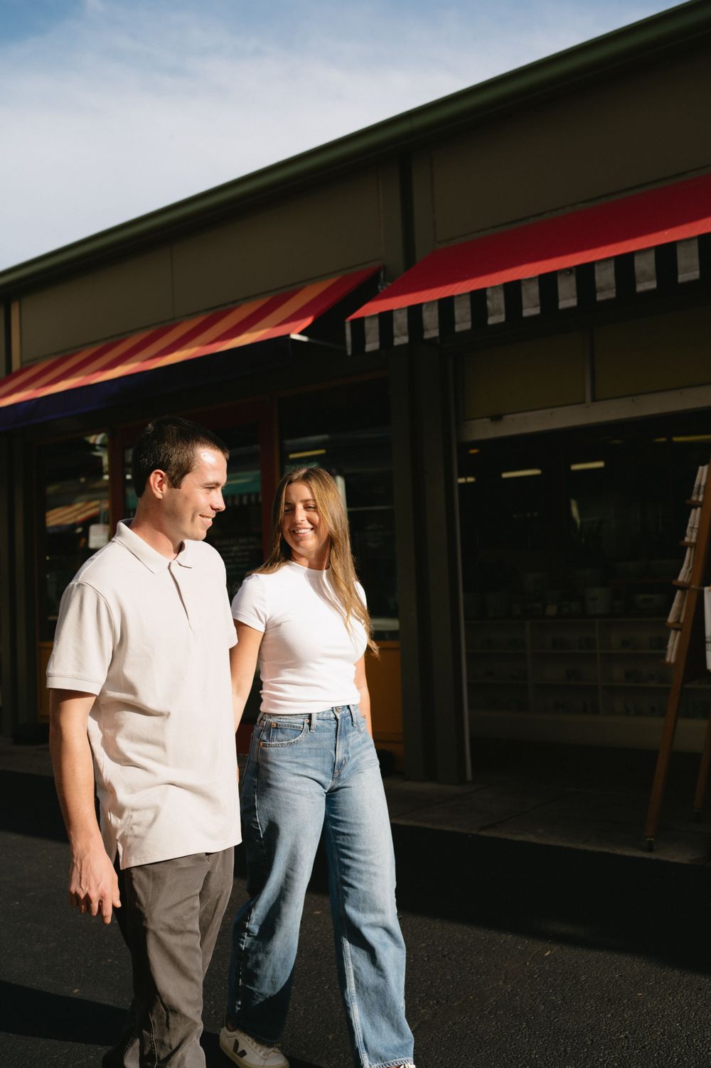 A couple stands together outside a storefront with red and white striped awnings.