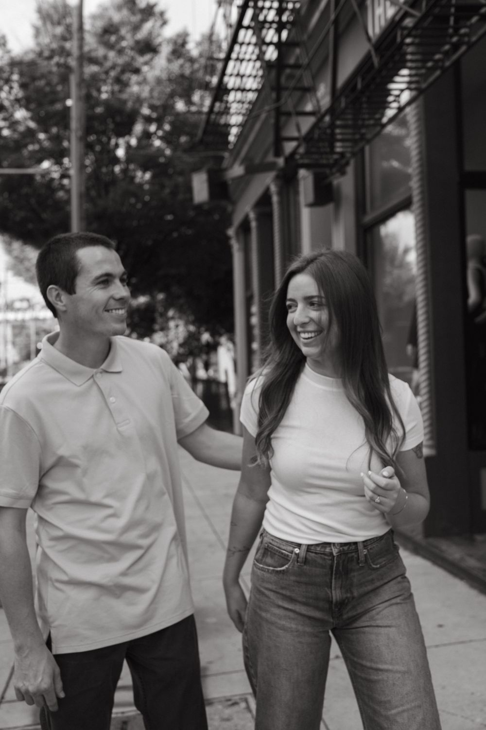 A couple walks together on a city sidewalk sharing a lighthearted moment.