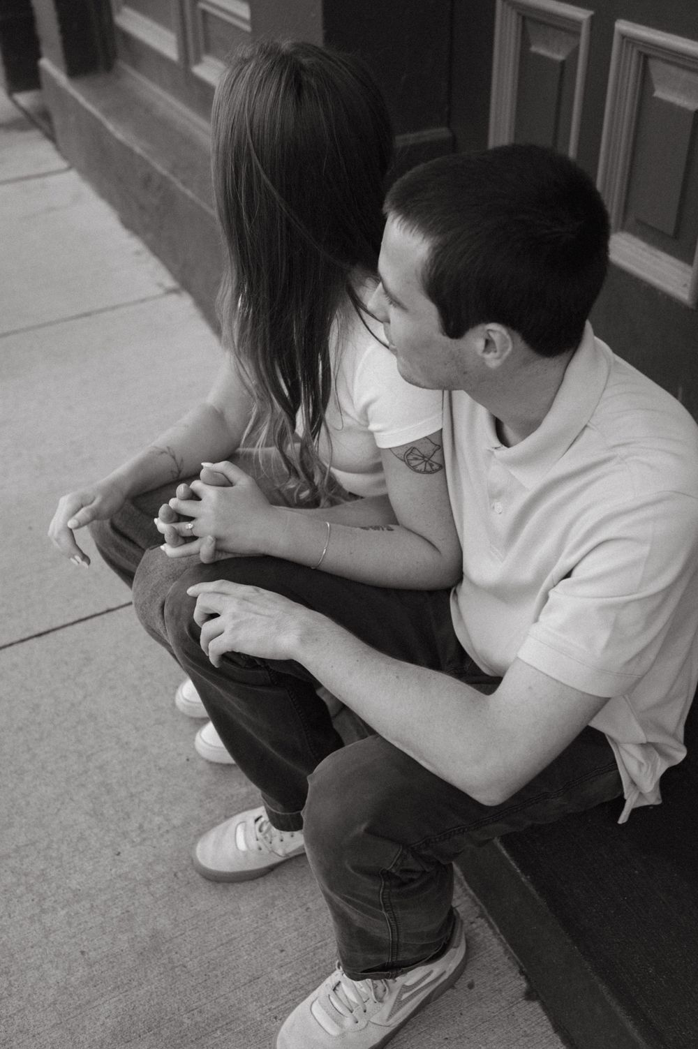 A black and white image of a couple sitting close together on outdoor steps.