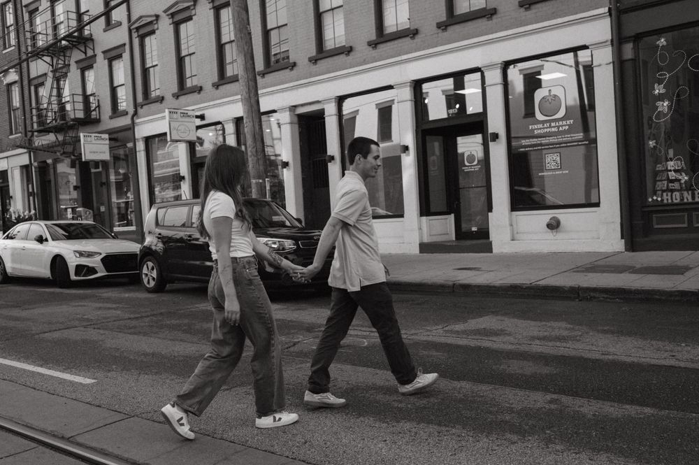 Couple walking hand in hand down a city street with vintage storefronts in black and white.