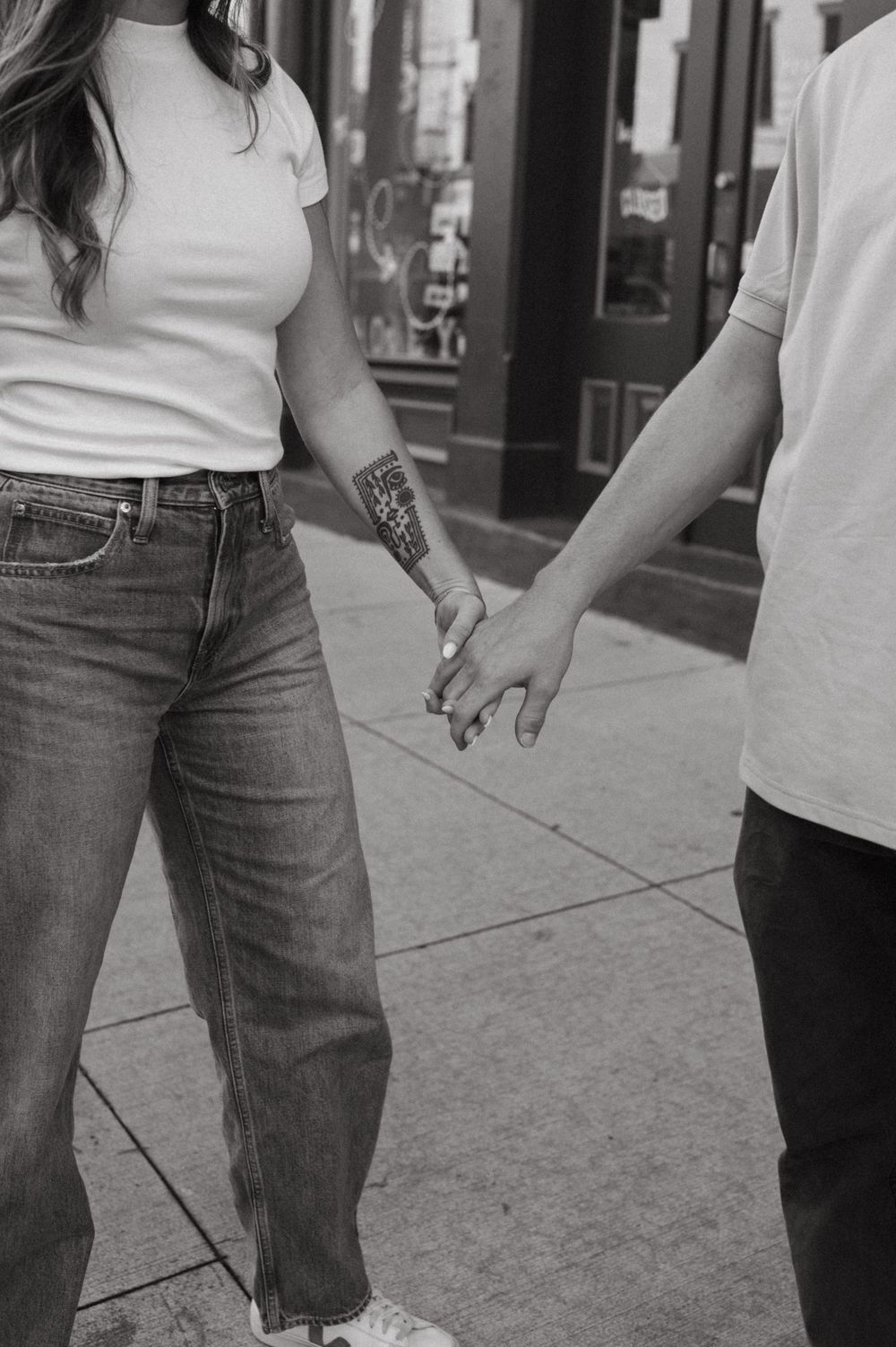 Close-up shot of two people holding hands while walking on a sidewalk, showing casual denim outfits.