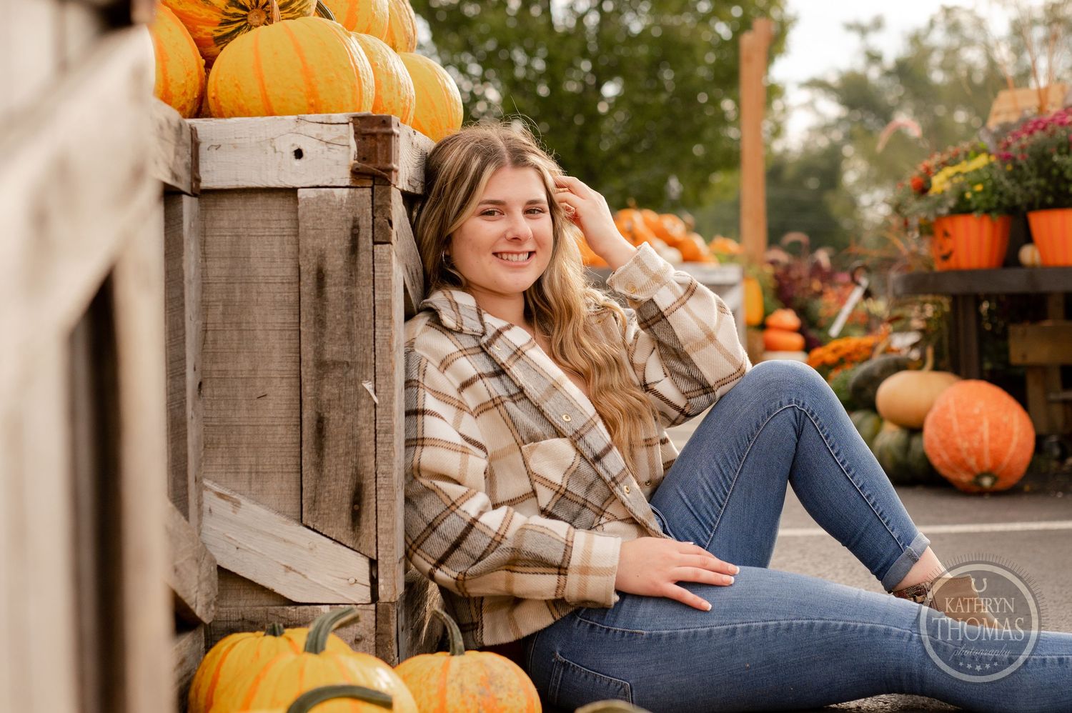 Casual autumn portrait with someone sitting among pumpkins and wooden crates at a market.