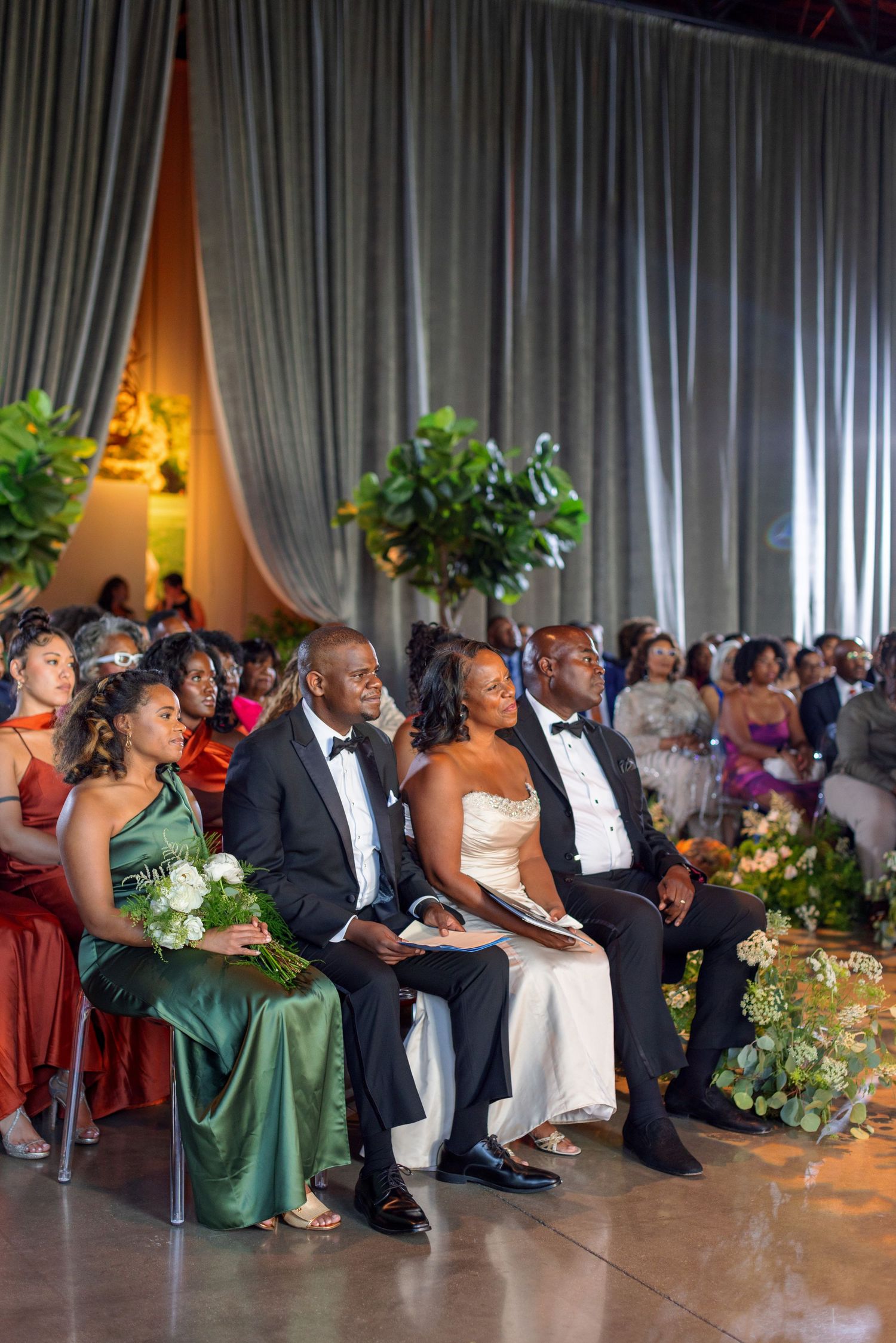 Wedding guests in formal attire seated in rows with colorful dresses and floral arrangements.