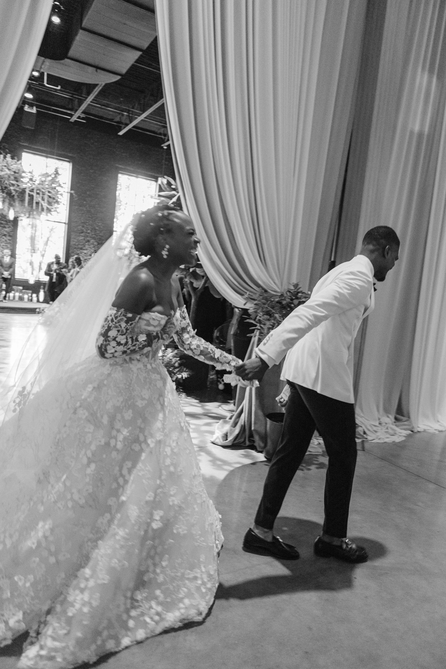 A playful wedding moment in black and white with elegant draping and natural lighting.