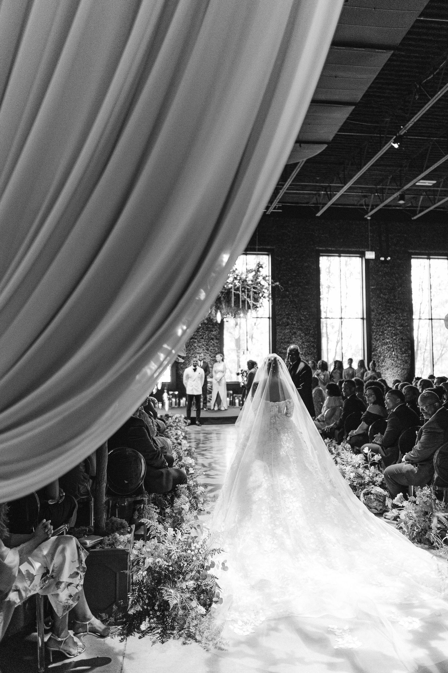 A stunning wedding ceremony with flowing white drapes and a cathedral-length veil in an elegant indoor venue.