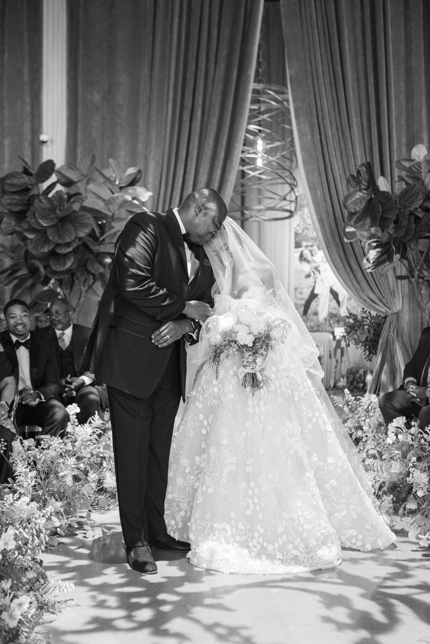 An intimate wedding moment captured in black and white with luxurious floral decorations and elegant draping.