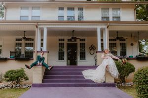 Wedding couple on purple steps in front of white colonial style building.