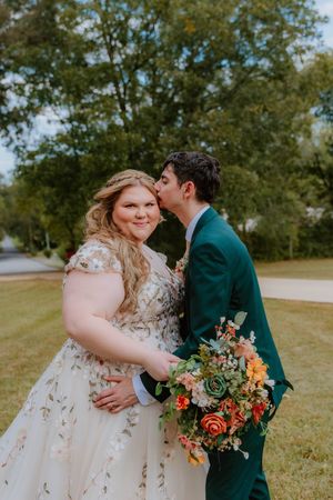 Couple embraces outdoors with a vibrant autumn bouquet featuring succulents and orange flowers.