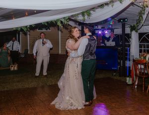 Wedding reception under draped fabric with guests dancing on wooden dance floor.