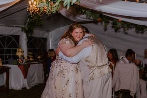 Wedding reception guests dancing under a draped tent ceiling with greenery decorations.
