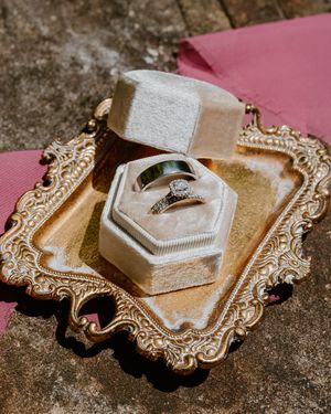 Wedding rings displayed on ornate vintage-style gold tray with hexagonal ring box.