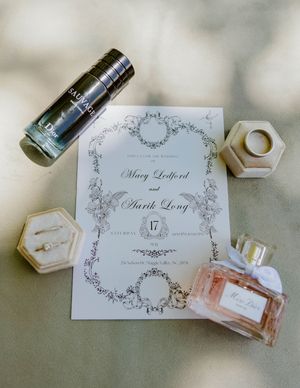Wedding invitations and perfume bottles arranged artistically on marble surface.