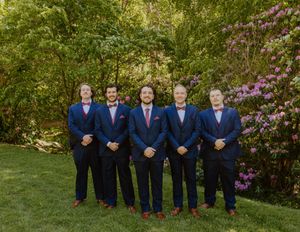 Groomsmen in navy suits lined up outdoors with pink flowering trees in background.