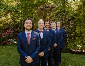 Wedding party in navy suits poses casually in front of blooming spring garden.