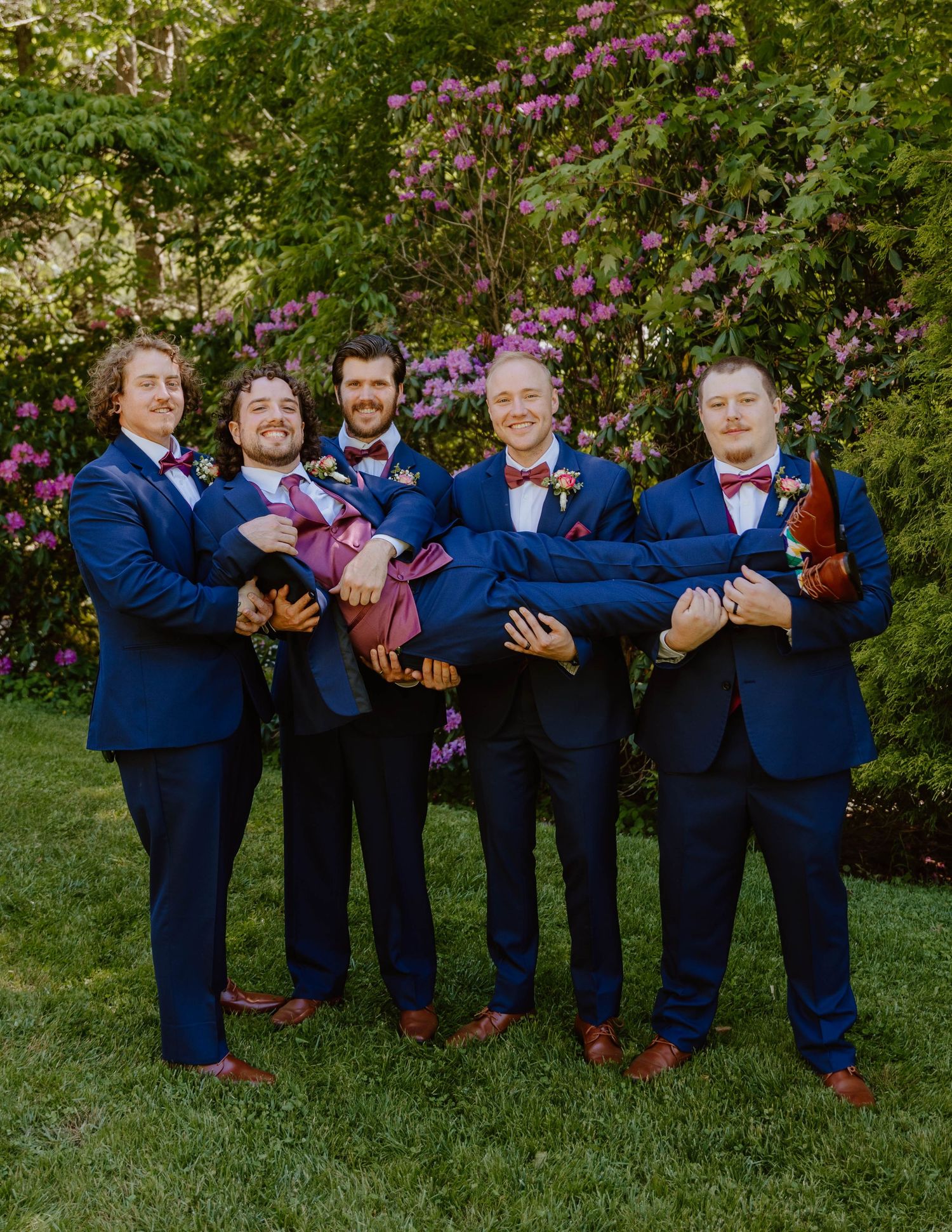 Groomsmen strike playful poses while lined up in navy suits with red bow ties.