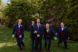 Wedding party members in navy suits strike dynamic poses outdoors in a garden setting.