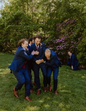 Group of people in navy suits perform synchronized jumping poses on a sunny lawn.