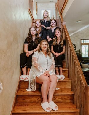 Bridesmaids in matching robes sit together on wooden stairs during wedding preparations.