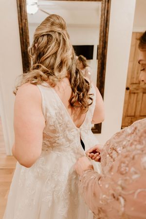 Wedding dress details showing intricate lace patterns and buttons in warm lighting.