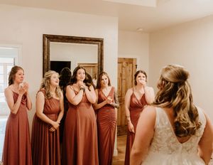 Row of bridesmaids in rust-colored dresses share emotional first look reactions.