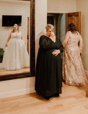 Wedding party members in formal attire gather in a bright indoor space with hardwood floors.