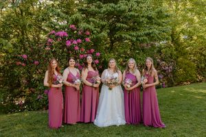 Wedding party poses on grassy lawn with pink flowering bushes in the background.