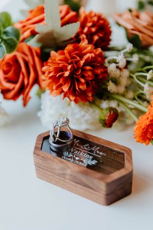Wedding rings displayed in wooden box with orange dahlias and white flowers.