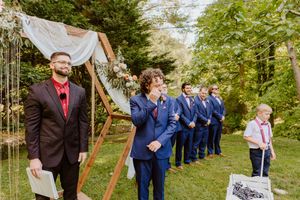 Wedding ceremony processional with groomsmen in navy suits walking down grassy aisle.