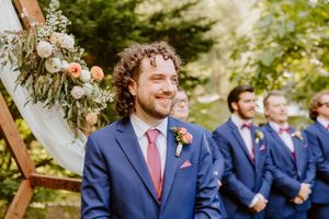 Groomsmen in navy suits and red ties gather under wooden wedding arch.
