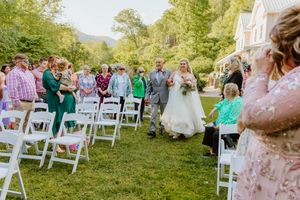 White folding chairs set up on lawn for outdoor wedding ceremony with guests seated.