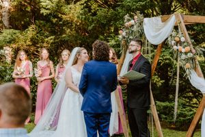Outdoor wedding ceremony with guests seated on white chairs and pink bridesmaids dresses.