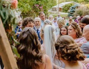 Wedding guests watching ceremony from white chairs in an outdoor garden setting.