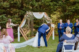 Garden wedding ceremony with decorative arch and white chairs arranged on grass.