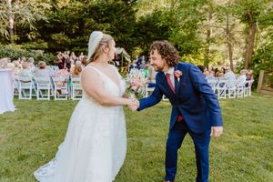 Wedding couple and bridal party dancing joyfully on a sunny outdoor lawn.