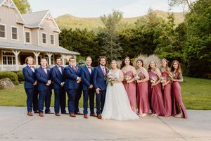Bridal party in navy and dusty rose attire posing together on a lawn with a house in background.