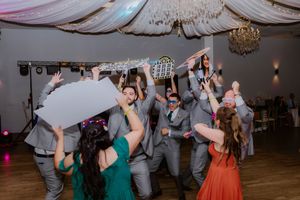 Wedding guests dancing and celebrating on a dance floor under elegant draped fabric and chandeliers.