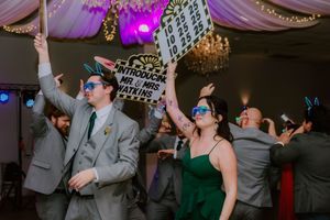 Wedding party dancing energetically under purple lighting at an indoor reception venue.