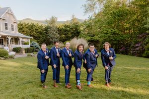 Groomsmen in matching navy suits and brown shoes posing playfully on lawn.