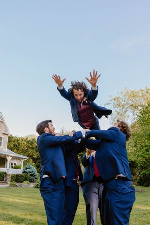 Playful groomsmen in navy suits jumping and posing outdoors for fun wedding photos.