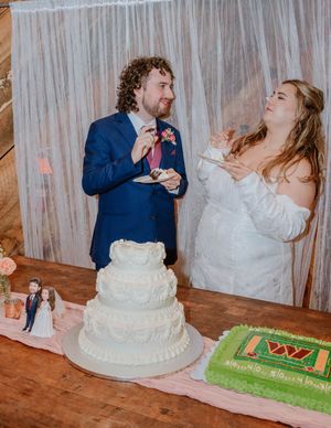 Newlyweds playfully smash wedding cake into each other's faces during reception celebration.