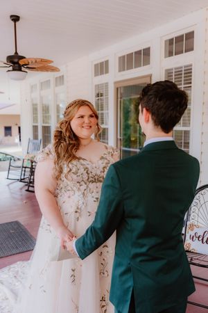 A couple shares a first look moment on a covered porch with white columns.