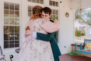 A wedding couple embraces on a white columned porch with rocking chairs.