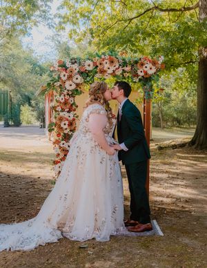 An outdoor wedding ceremony setup with floral arch and natural woodland backdrop.