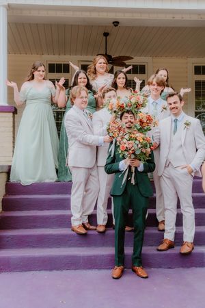 Wedding party poses on purple steps wearing mix of sage green and light colored formal attire.