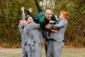 Groomsmen in matching gray suits posing playfully outdoors during autumn.