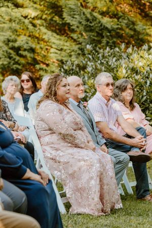 Wedding guests seated on white chairs during outdoor ceremony.