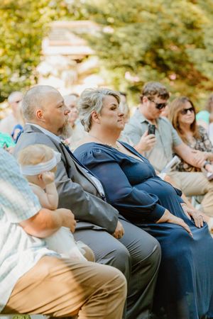 Wedding guests watching ceremony from white chairs on sunny lawn.