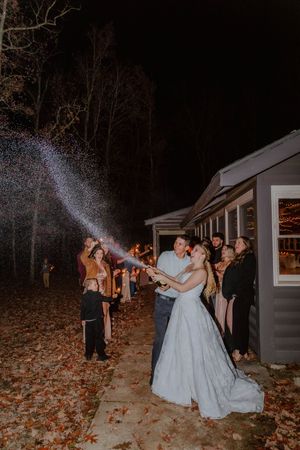 Wedding celebration with champagne spraying in the dark against rustic building backdrop.