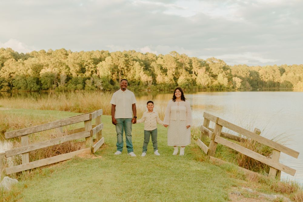 Family photo session by wooden fence overlooking scenic lake at sunset.