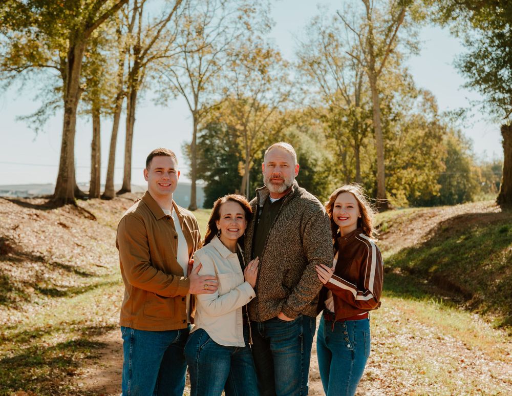 Family portrait on a scenic autumn trail with golden sunlight filtering through trees.